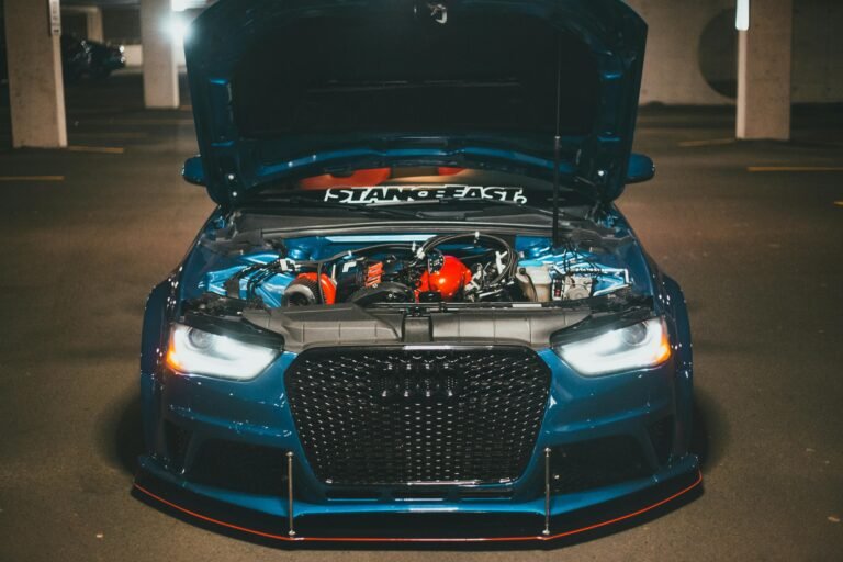 Blue sports car with open hood displaying engine in dimly lit urban setting.